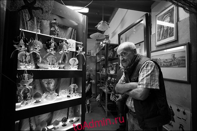 Пожилой мужчина со скрещенными руками в магазине сувениров